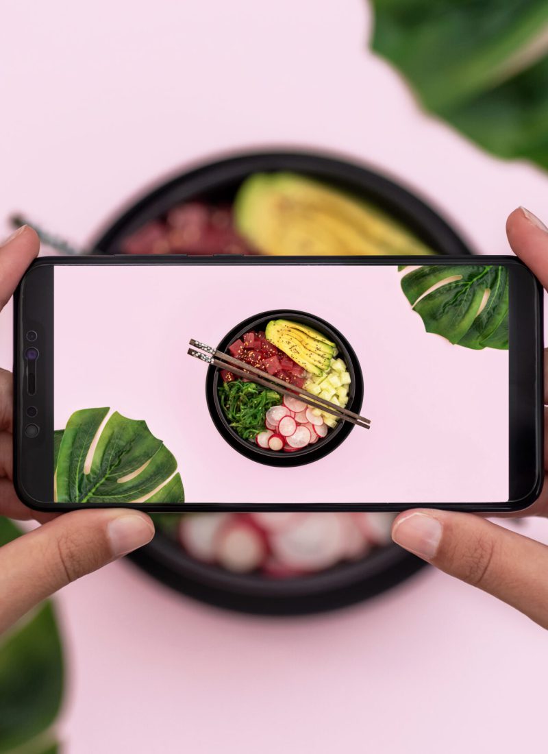 Top view of woman taking picture of tuna poke bowl on pink background