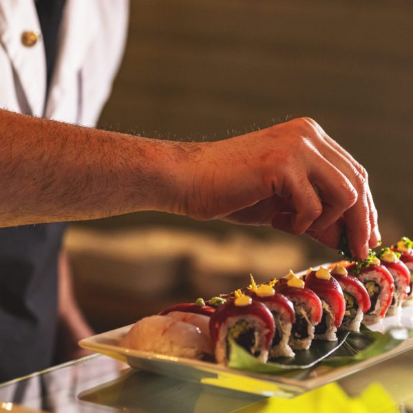 Professional sushi chef decorating sushi rolls preparing to be served on plate at commercial kitchen.